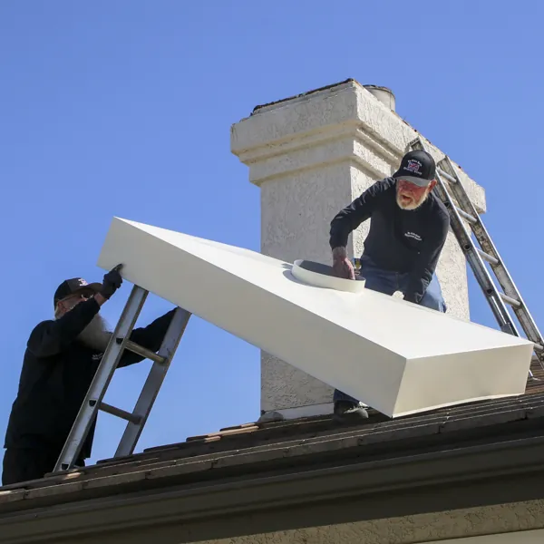 Two members of the crew lifting a new chase cover into place under a chimney stack