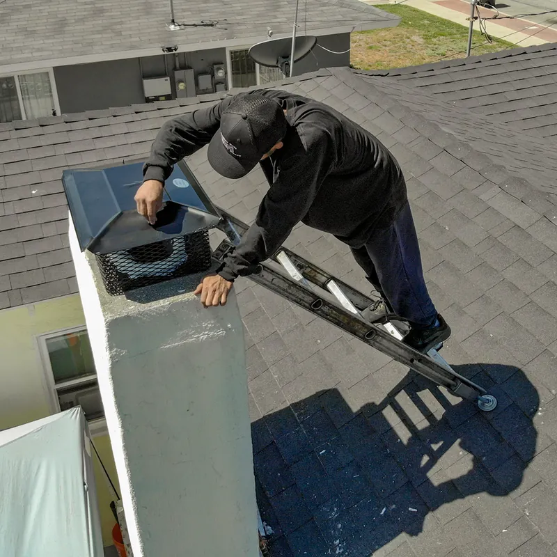 A technician on a ladder fitting a new cap on a chimney